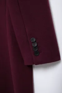 Détail de manche de manteau en mélange de laine femme en bordeaux profond avec boutons.