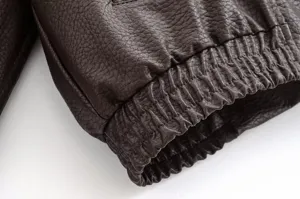 Détail de manche de veste en cuir marron foncé, texture litchi claire et poignet côtelé.