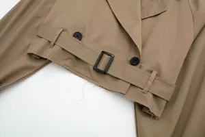 Close-up detail of women's cropped khaki trench coat featuring waist belt and raw hem.