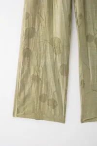 Détail de pantalon plissé vert montrant un tissu léger et un motif imprimé floral.
