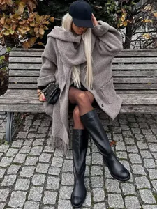 Detail shot of the cozy grey knitted hooded coat and matching scarf worn outdoors on a bench.