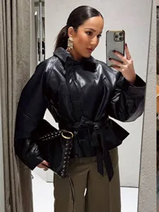 Detail shot of a black faux leather jacket with belt, worn in a stylish mirror selfie setup.