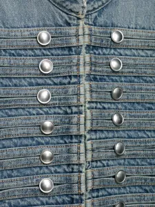 Detailopname van een stijlvolle spijkerjas met metalen knopen en plooidetails.