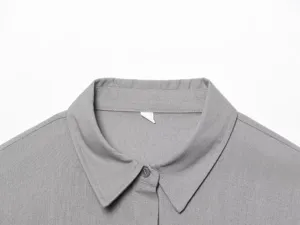Dettaglio colletto camicia manica lunga grigia, camicetta casual in tinta unita con bottoni.