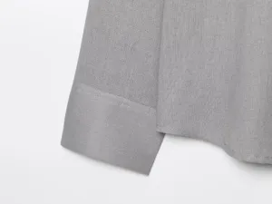 Dettaglio in primo piano del polsino della camicia grigia con tessuto fine e cuciture.