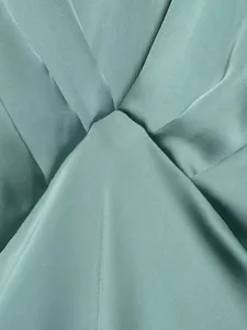 Close-up detail of elegant green satin dress featuring smooth fabric texture and pleats.