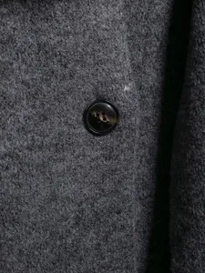 Close-up detail of dark grey woolen coat fabric and classic button texture, soft and warm.