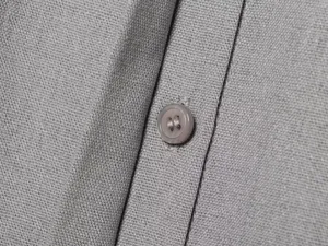 Primo piano dettagliato della trama del tessuto grigio e del bottone coordinato sulla camicia.