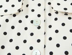 Close up detail of women elegant white long sleeve shirt featuring classic black polka dots.