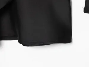 Close-up detail shot of smooth black satin fabric garment featuring fine stitching and elegant texture.