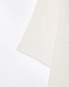 Gros plan de la manche de cardigan en tricot blanc avec texture fine et poignet côtelé.