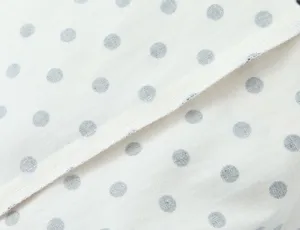 Close-up detail of white fabric with black polka dots and fine stitching seam design.