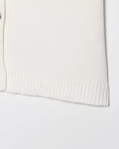 Gros plan détaillé du gilet en tricot blanc pour femme avec ourlet côtelé et patte de boutons.