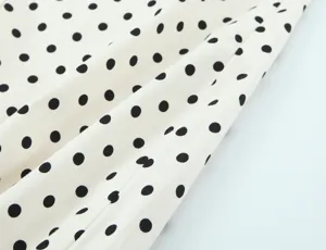 Detailed view of white fabric with classic black polka dots, showing fine texture.