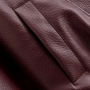 Détail de poche de veste en cuir gros plan montrant texture litchi bordeaux et coutures.