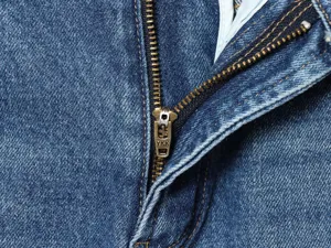 Primo piano dettaglio di cerniera lampo anteriore e ferramenta metallica per jeans.