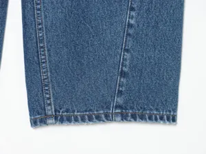 Primo piano dettagliato di jeans blu con cuciture a contrasto e orlo sfrangiato.