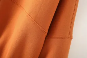 Close-up detail shot of orange women's jacket hoodie fabric showing fine stitching texture.