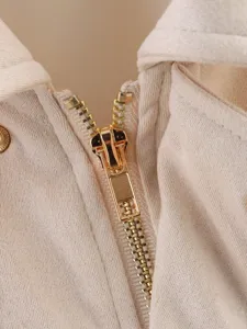 Gros plan détaillé sur la fermeture éclair dorée métallique d'une veste pilote en polaire beige.