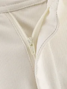 Close up of white garment zipper detail showing textured fabric and embossed metal pull.