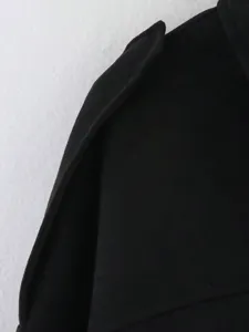 Gros plan sur l'epaule de la veste en daim noir montrant la texture fine du tissu.