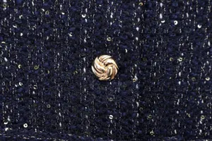 Close-up detail of dark blue sequin tweed fabric featuring an intricate metallic gold button.
