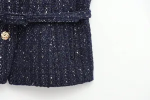 Close-up detail of dark blue textured tweed fabric featuring metallic buttons and matching belt.
