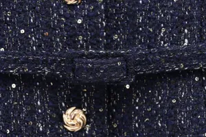 Close-up detail of dark blue tweed textured fabric with metallic sequins and gold buttons.