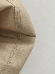 Detailed view of fine stitching and hem on a beige dress, showing quality craftsmanship.