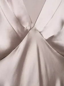 Close-up detail of women's elegant satin V-neck dress, showcasing smooth glossy fabric.