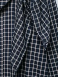 Close-up detail of navy blue and white plaid shirt fabric showing the elegant necktie bow.