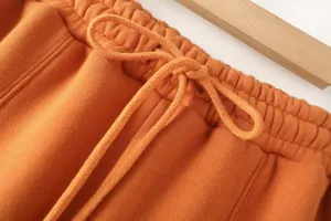 Close-up detail of orange casual sweatpants with elastic drawstring waistband, soft knit fabric.