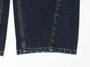 Primo piano dell'orlo dei jeans blu scuro con cuciture a contrasto e dettaglio.