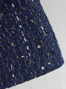 Close-up detail of luxury tweed jacket fabric with glittering sequins and metallic threads.