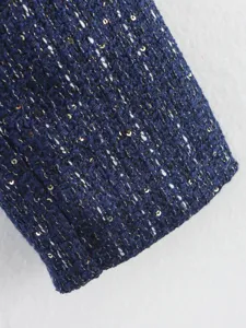 Detailed closeup view of womens blue tweed jacket sleeve featuring gold sequins and texture.
