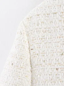 Close-up detail of white tweed jacket fabric with shimmering gold sequins and fine woven texture.