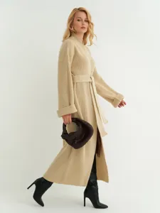 Lang beige gebreid vest detail, gezellige losse wintertruijas met riem gedragen door model.