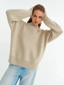 Dettaglio di un maglione in maglia beige da donna con maniche lunghe e scollo a girocollo a costine.