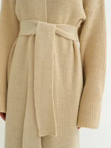 Detail van lang beige gebreid damesvest met comfortabele textuur en bijpassende riem.