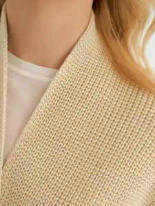 Close-up detail van een beige grof gebreide cardigan trui met mooie kraag textuur.