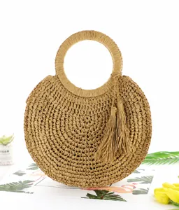 Dettaglio ravvicinato di elegante borsa a mano rotonda in paglia intrecciata con nappina.