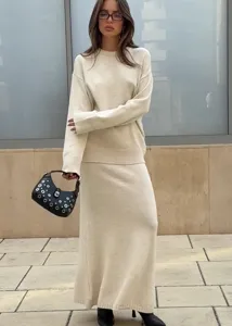 Vue détaillée du pull en tricot beige ample et de l'ensemble de jupe dans un décor extérieur.