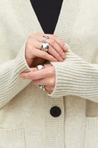 Primer plano detallado de elegantes anillos de plata usados en tela de cárdigan acogedora.