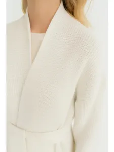 Close-up detailweergave van de witte gebreide vesttextuur, zachte stof en bijpassende riem.