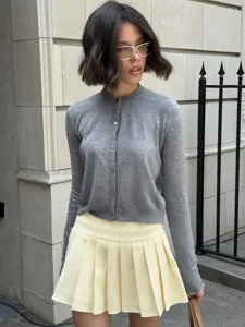 Detailansicht der grauen Strickjacke mit Knöpfen für Damen und dem gelben Faltenrock.