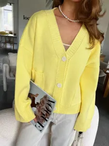 Detalle de cárdigan de punto amarillo con cuello en V, bolsillos y botones para estilo otoñal.