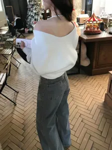 Detail view of a stylish off-shoulder V-neck knit sweater worn by a woman in a room.