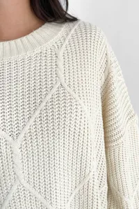 Detaillierte Nahaufnahme der cremeweißen Zopfmuster Strickpullover Textur weich.