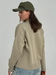 Vista detallada de cárdigan de punto para mujer en estilo informal, con gorra verde y vaqueros.