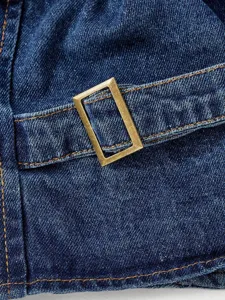 Close-up detail of dark blue denim fabric featuring contrast stitching and metal buckle.